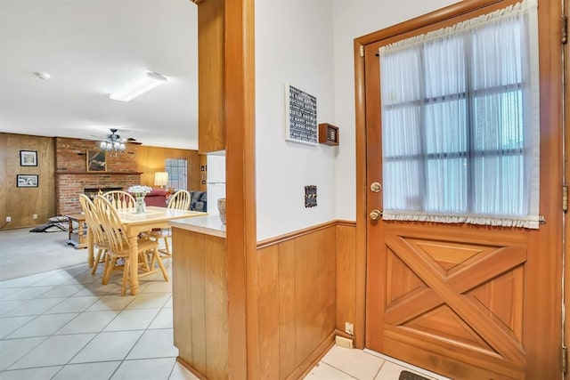 entryway with ceiling fan, wooden walls, light tile patterned floors, and a brick fireplace