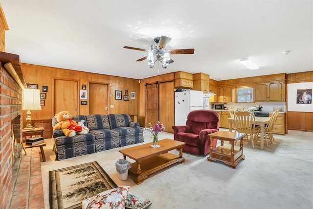 living room featuring ceiling fan, a barn door, a fireplace, and wooden walls