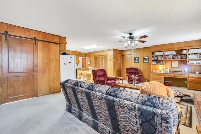 carpeted living room with a barn door, ceiling fan, and wooden walls