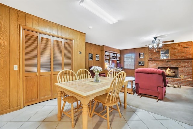 dining area with wood walls, a fireplace, ceiling fan, and light tile patterned floors