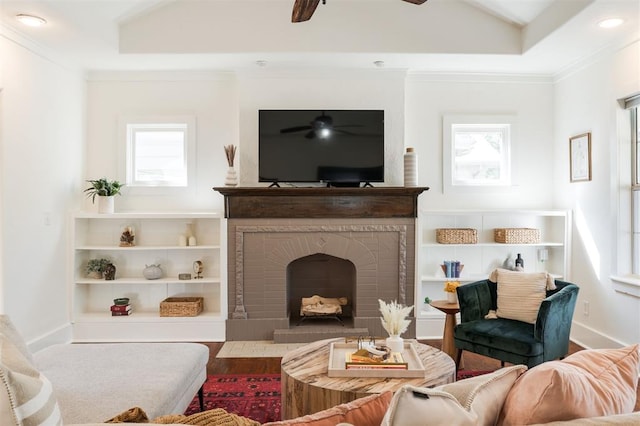 living room with a brick fireplace, vaulted ceiling, ceiling fan, crown molding, and wood-type flooring