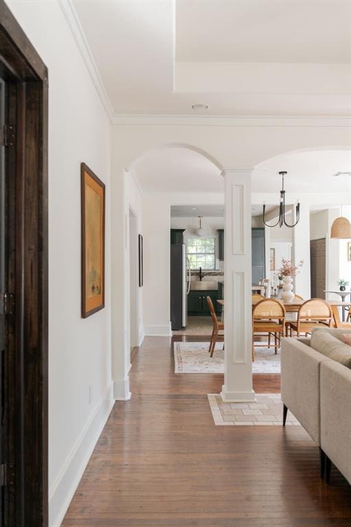 hall with ornate columns, crown molding, a notable chandelier, and hardwood / wood-style flooring