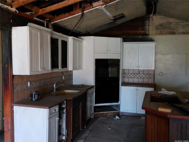 kitchen featuring dobule oven black, tasteful backsplash, white cabinetry, and a sink