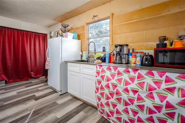 kitchen featuring sink, light hardwood / wood-style flooring, a textured ceiling, white fridge, and white cabinetry