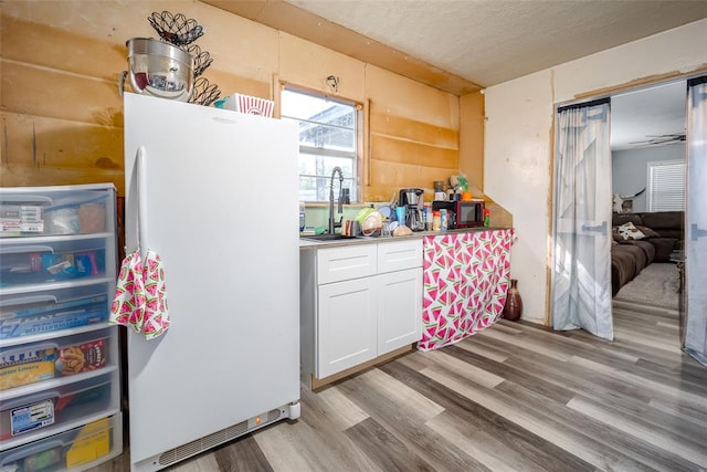 kitchen featuring white cabinetry, sink, white fridge, light hardwood / wood-style floors, and a textured ceiling