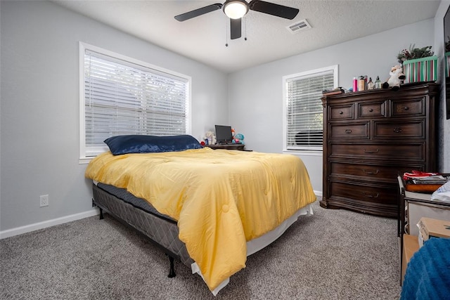 bedroom featuring a textured ceiling, light colored carpet, multiple windows, and ceiling fan