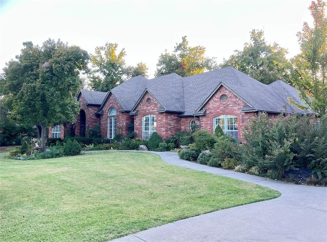 view of front facade with roof with shingles, a front lawn, and brick siding