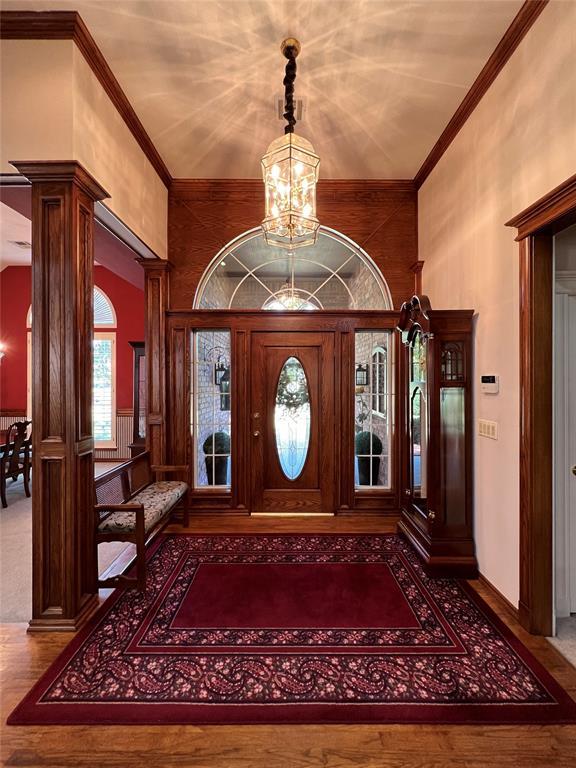 entrance foyer featuring baseboards, ornamental molding, wood finished floors, an inviting chandelier, and ornate columns