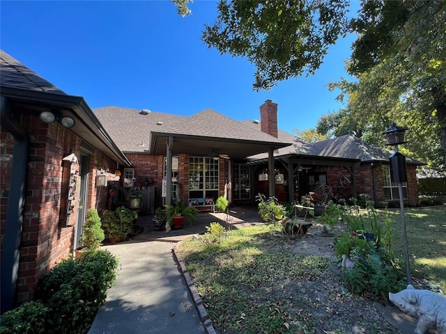 rear view of house with a ceiling fan, a chimney, roof with shingles, a patio area, and brick siding