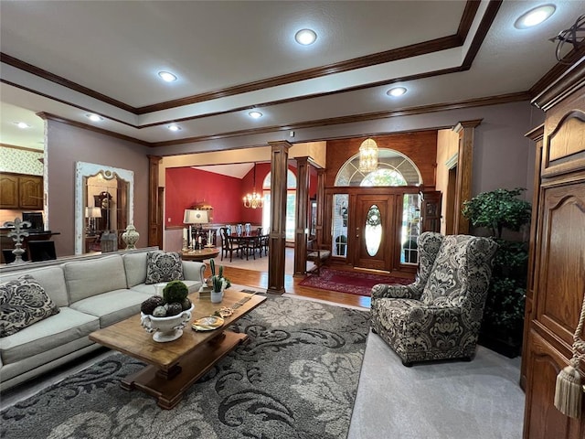 living area featuring a tray ceiling, crown molding, recessed lighting, an inviting chandelier, and ornate columns