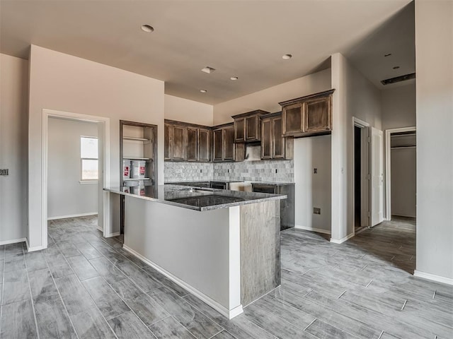 kitchen with dark stone countertops, backsplash, dark brown cabinets, and a center island