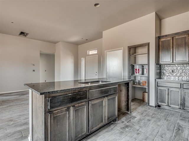 kitchen featuring dark brown cabinetry, an island with sink, and dark stone counters