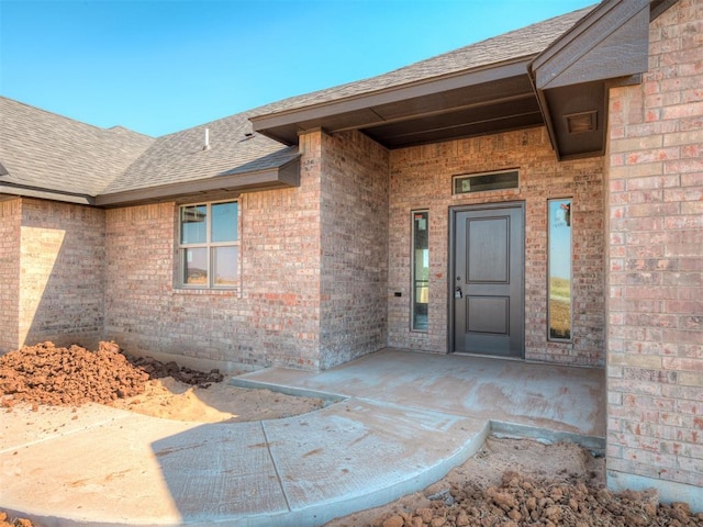 entrance to property featuring brick siding and a shingled roof