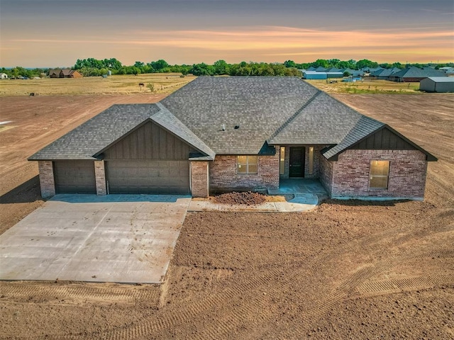 view of front of house with a garage, driveway, board and batten siding, brick siding, and roof with shingles