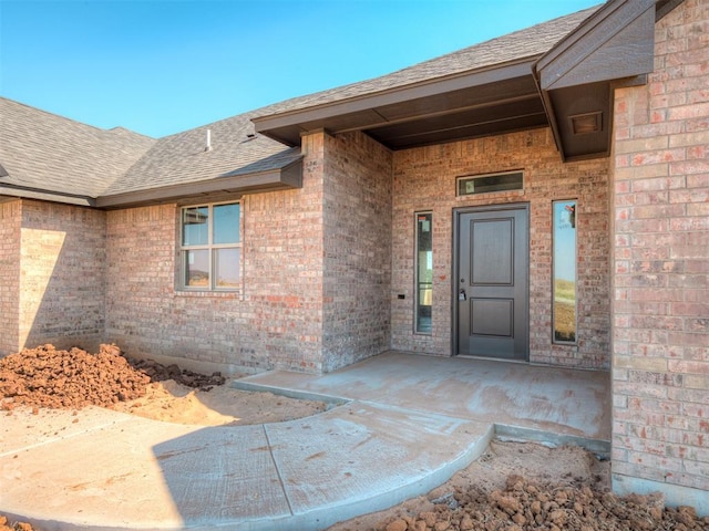 doorway to property featuring roof with shingles and brick siding