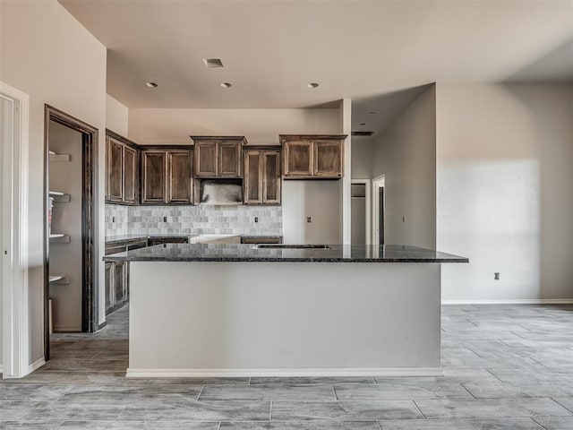 kitchen with a kitchen island, light wood-style flooring, dark stone countertops, dark brown cabinetry, and decorative backsplash