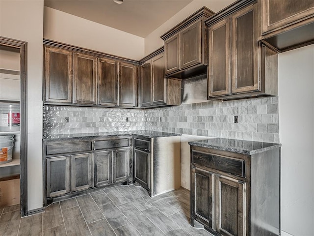 kitchen featuring backsplash, dark brown cabinets, wood finished floors, and dark stone countertops