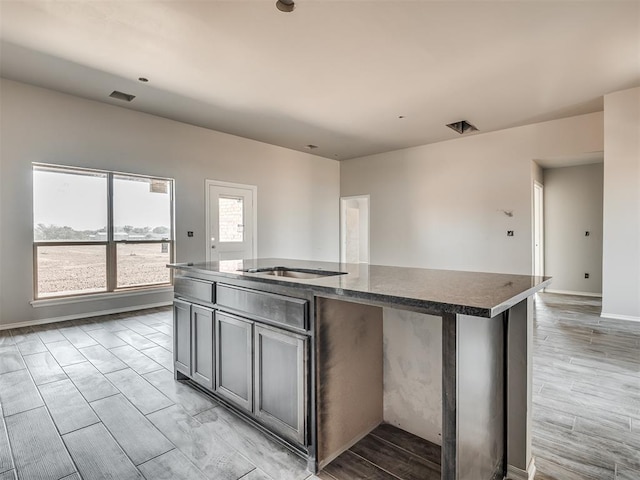 kitchen with baseboards, visible vents, a center island with sink, light wood-type flooring, and gray cabinets