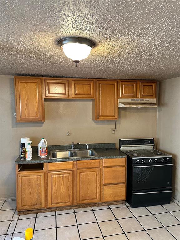 kitchen with a textured ceiling, black electric range oven, light tile patterned floors, and sink