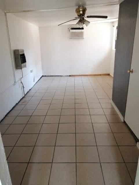 empty room with a wall unit AC, heating unit, ceiling fan, and tile patterned flooring