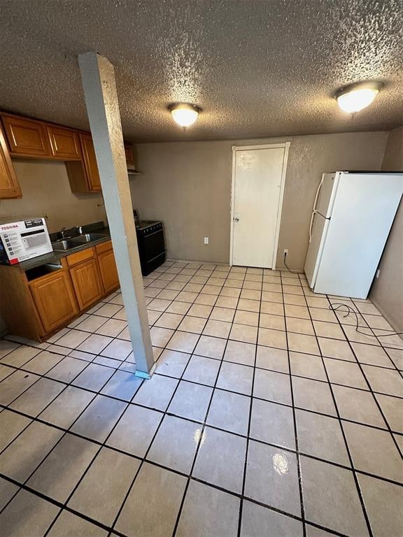 kitchen featuring white fridge, sink, light tile patterned floors, and a textured ceiling