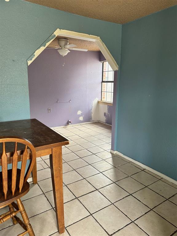 unfurnished dining area featuring ceiling fan, light tile patterned floors, and a textured ceiling