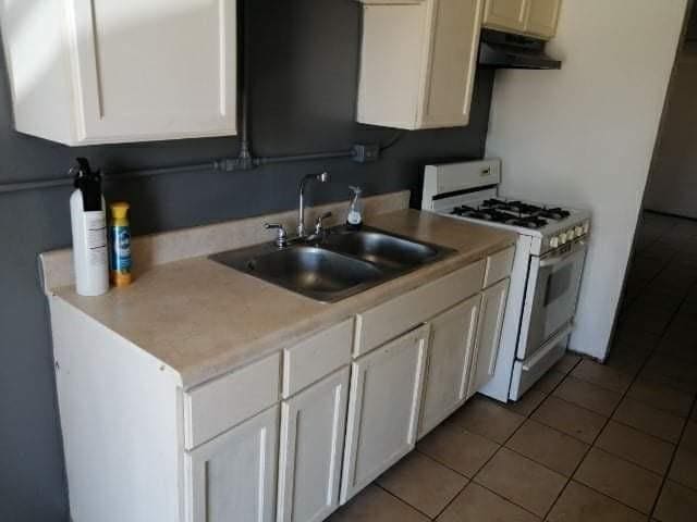 kitchen featuring white cabinets, tile patterned floors, white gas stove, and sink