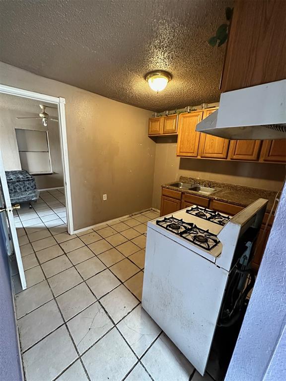 kitchen featuring a textured ceiling, ventilation hood, ceiling fan, light tile patterned floors, and white gas stove