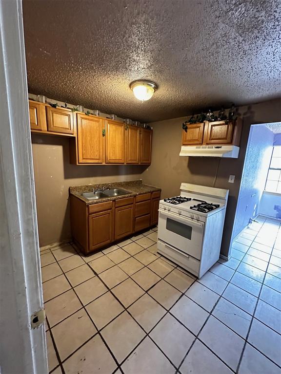 kitchen featuring white gas stove, light tile patterned floors, a textured ceiling, and sink