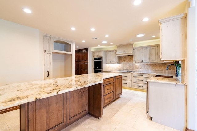 kitchen with light stone countertops, sink, cream cabinetry, a kitchen island, and custom exhaust hood