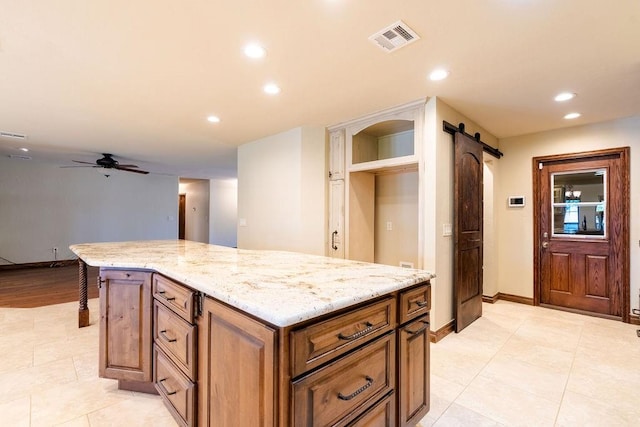 kitchen featuring a barn door, ceiling fan, a kitchen island, and light stone countertops