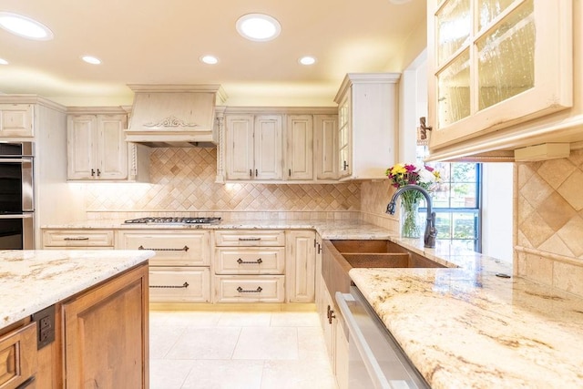 kitchen featuring light stone countertops, custom range hood, stainless steel appliances, sink, and light tile patterned flooring