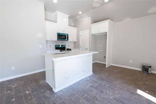 kitchen with white cabinetry, sink, decorative backsplash, a center island with sink, and stainless steel range oven