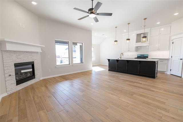 kitchen with pendant lighting, sink, white cabinets, stainless steel range, and a center island with sink