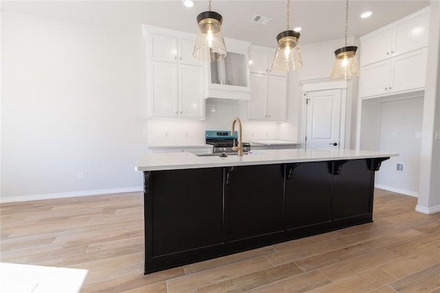 kitchen featuring white cabinetry, decorative light fixtures, and a kitchen island with sink