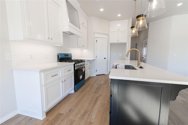 kitchen featuring white cabinets, a center island with sink, hanging light fixtures, and stainless steel gas range oven