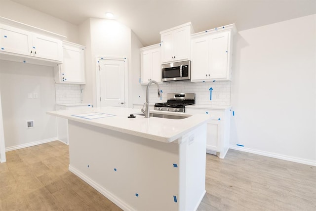 kitchen with appliances with stainless steel finishes, white cabinets, a sink, and a center island with sink