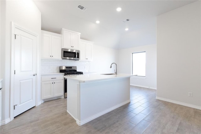 kitchen with visible vents, stainless steel appliances, lofted ceiling, a sink, and backsplash