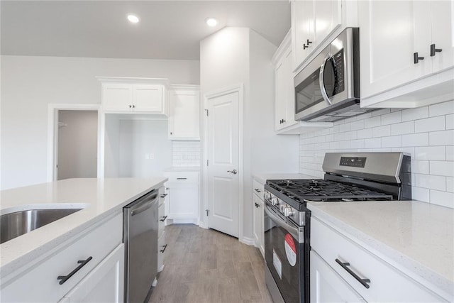 kitchen with recessed lighting, light wood-type flooring, white cabinets, light stone countertops, and appliances with stainless steel finishes
