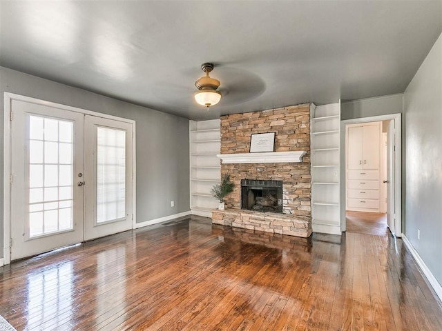 unfurnished living room featuring french doors, a stone fireplace, ceiling fan, built in features, and wood-type flooring