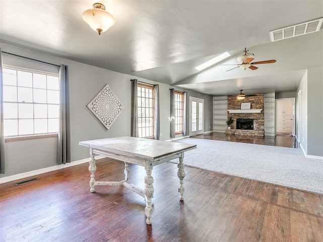 recreation room with hardwood / wood-style flooring, ceiling fan, vaulted ceiling with skylight, and a fireplace