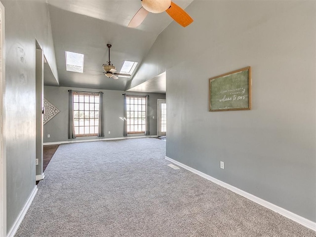 empty room featuring a skylight, ceiling fan, carpet floors, and high vaulted ceiling