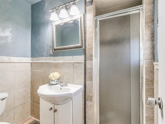 bathroom featuring vanity, toilet, a shower with door, and tile walls