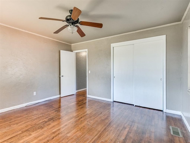 unfurnished bedroom featuring ceiling fan, a closet, wood-type flooring, and ornamental molding