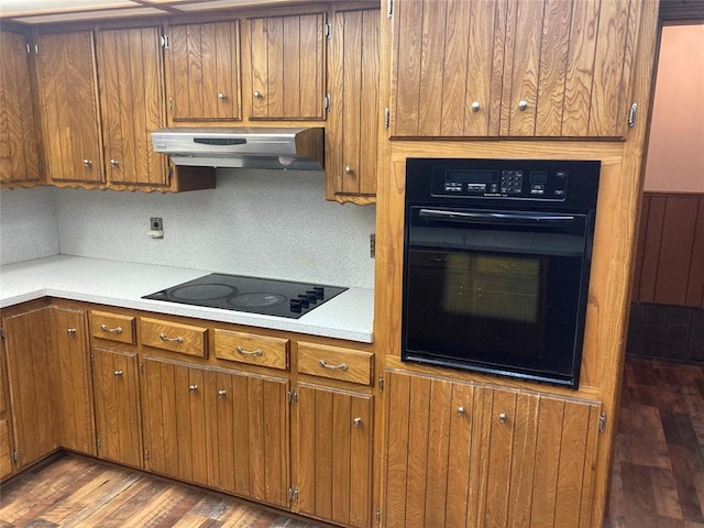 kitchen with backsplash, dark wood-type flooring, black appliances, and range hood