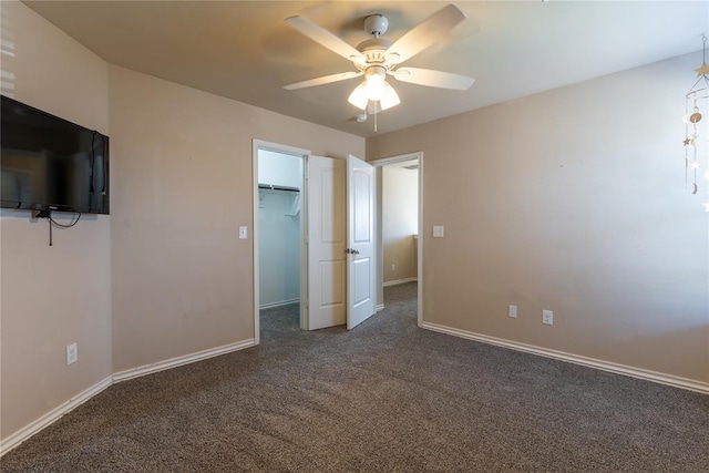 unfurnished bedroom featuring a walk in closet, ceiling fan, a closet, and dark carpet