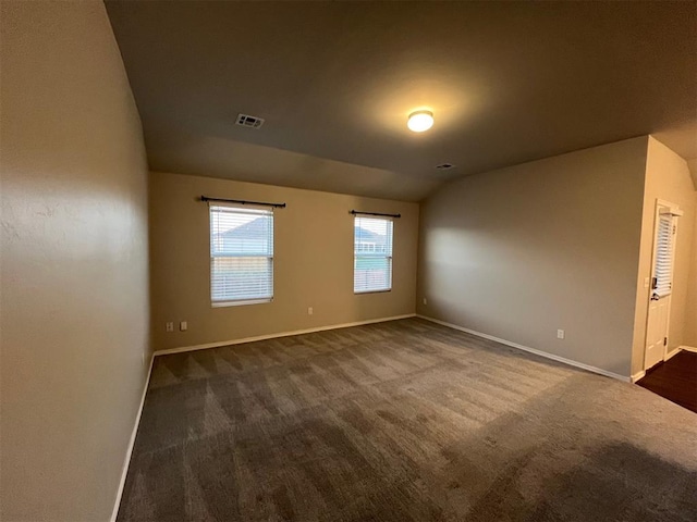 spare room featuring dark carpet and lofted ceiling