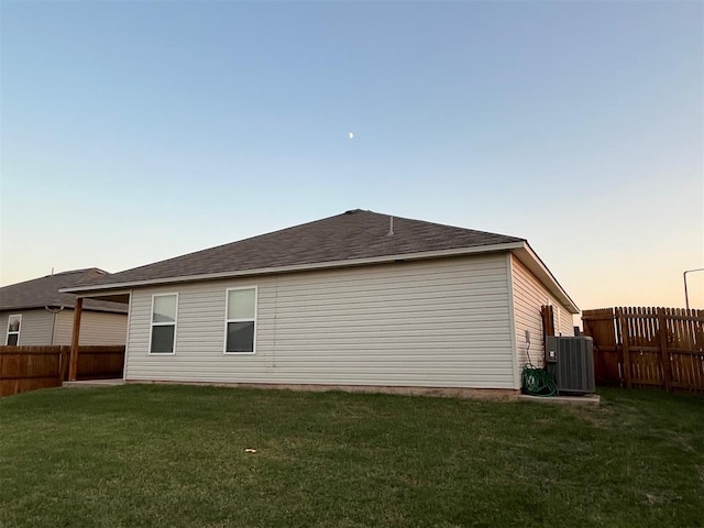 property exterior at dusk with central AC unit and a lawn