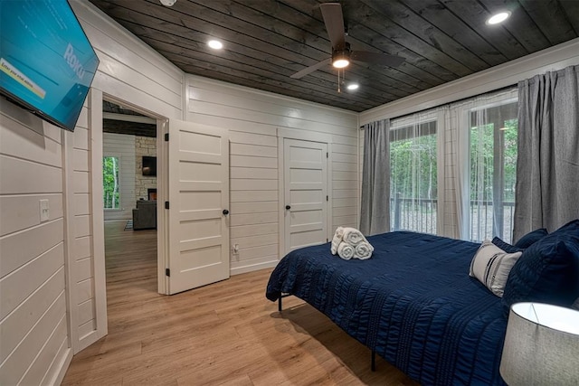 bedroom with access to outside, wooden walls, ceiling fan, and light hardwood / wood-style floors