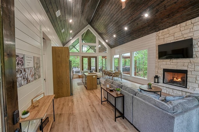 living room featuring wooden ceiling, a stone fireplace, light hardwood / wood-style flooring, high vaulted ceiling, and beamed ceiling